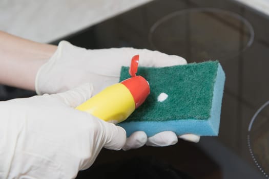Cleaning of the kitchen hob. Woman is applying a cleaner to a sponge.