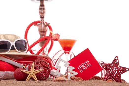 Beach accessories, seashells, sand, glass with cocktail, hookah (shisha) and christmas ornaments on white background. New Year and Christmas. Winter vacation in warm countries, beach holiday