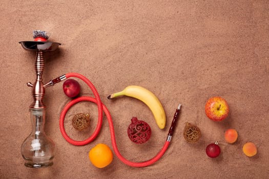 Hookah (shisha), fruit and christmas ornaments on sand background. Top view. New Year and Christmas. Winter vacation in warm countries, beach holiday