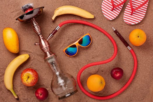 Beach accessories, hookah (shisha) and fruit on sand background. Top view. Vacation in warm countries, Beach party and holiday