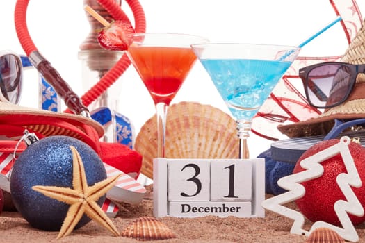 Beach accessories, seashells, sand, two glasses of cocktail, hookah (shisha) and christmas ornaments on white background. New Year. Winter vacation in warm countries, beach holiday