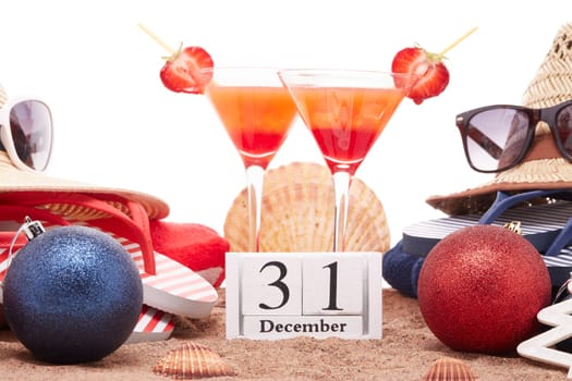 Beach accessories (flip flops, straw hats, seashells, sand, sunglasses), two glasses of cocktail, christmas ornaments on white background. New Year. Winter vacation in warm countries, beach holiday