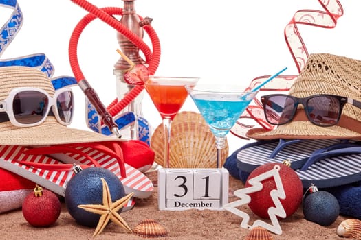 Beach accessories, seashells, sand, two glasses of cocktail, hookah (shisha) and christmas ornaments on white background. New Year. Winter vacation in warm countries, beach holiday