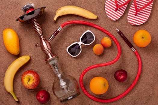Beach accessories, hookah (shisha) and fruit on sand background. Top view. Vacation in warm countries, Beach party and holiday