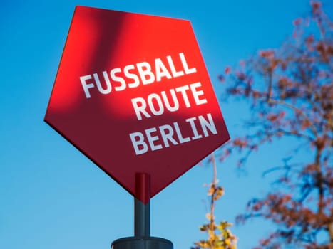 Red pentagonal sign with the inscription FOOTBALL ROUTE BERLIN in front of blue sky in Berlin-Frohnau. These signs lead right through Berlin's football training courses.