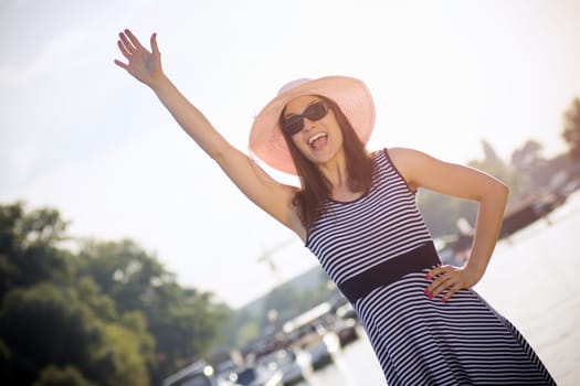 The attractive woman in summer clothing is waving outdoors and says Hello.