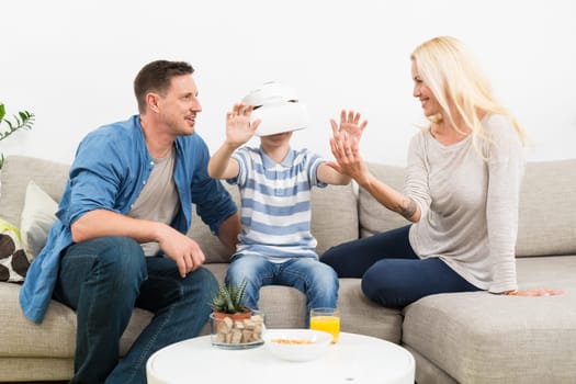 Happy caucasian family at home on living room sofa having fun playing games using virtual reality headset.