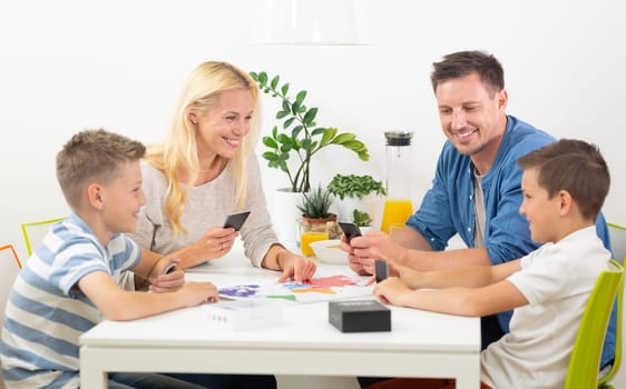 Happy young family playing card game at dining table at bright modern home. Spending quality leisure time with children and family concept. Cards are generic and debranded.