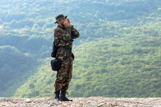 The man in military uniform is shouting in the nature on green background.