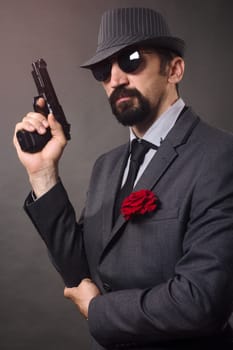 The old-fashioned elegant man in suit, hat and sunglasses is holding a pistol in hand.