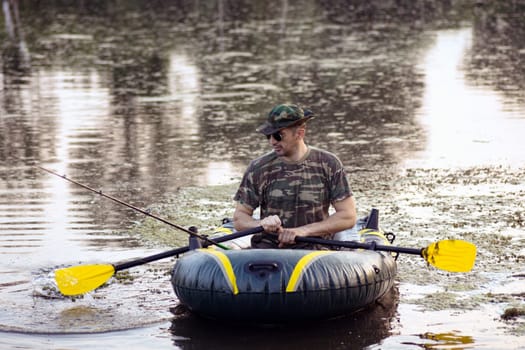 The fisherman is fishing on the lake from inflatable boat.