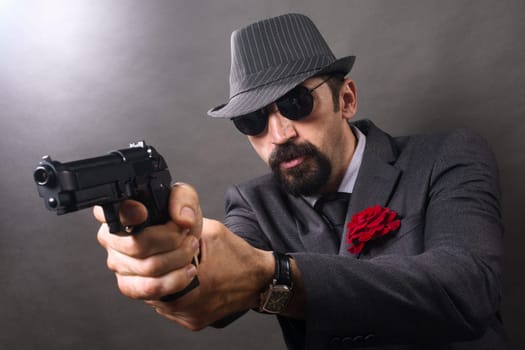The gangster in elegant suit and hat in vintage style is aiming with pistol.