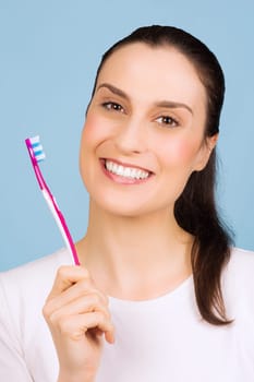 Beautiful smiling woman is holding a toothbrush on blue background.