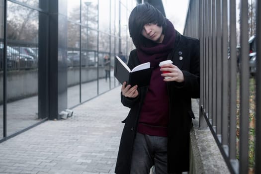 The trendy student is learning, studying, reading a book and drinking coffee at the street.