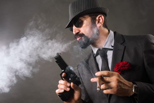 The elegant mafia boss or gangster is smoking cigar and holding pistol in hand.