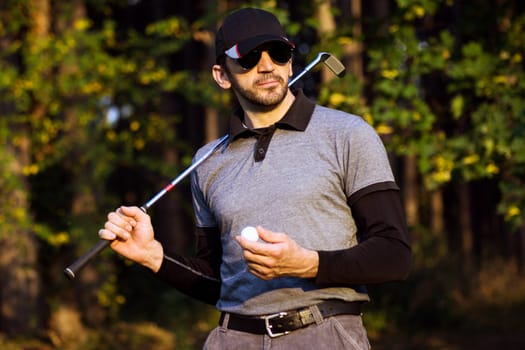 Portrait of golfer or golf player with golf stick and golf ball in hand in nature on golf course.