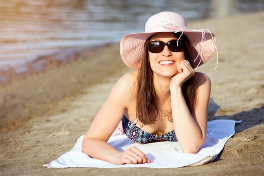 The attractive smiling woman is sunbathing on the beach and enjoying in summer.