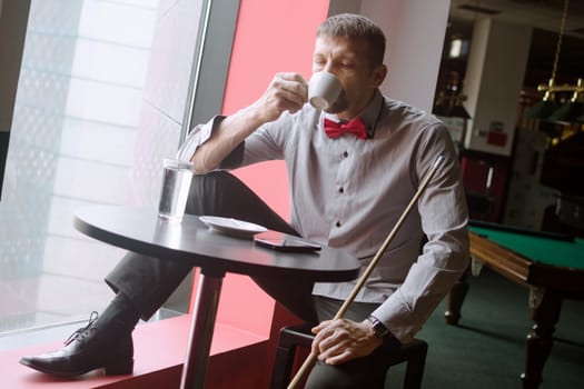 The billiard player is drinking coffee in billiard club.