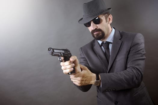 The old-fashioned elegant man is holding a pistol in his hands on gray background.