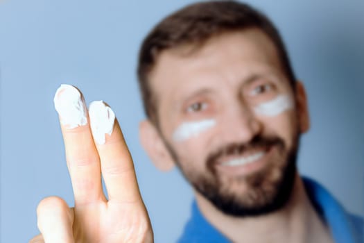 The moisturizer or cream for skin is on fingers of man on blur background, skincare for men.