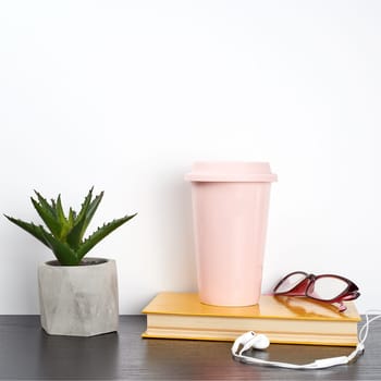 closed book and pink ceramic glass with coffee on a black table, white wall