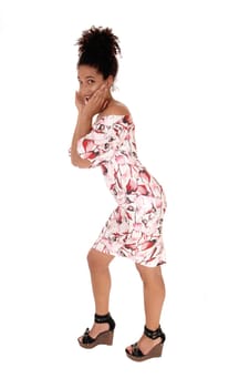 A gorgeous young multi-racial woman standing in a summer dress.in profile, with her hands on her face and black.curly hair in a bun, isolated for white background.