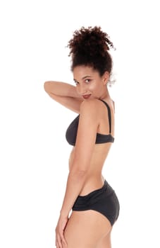 A beautiful slim young multi-racial woman standing in profile in a black.bikini in the studio with her curly black hair in a.bun on her head, isolated for white background.