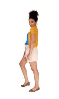 Beautiful young multi-racial woman standing in shorts and a yellow.sweater in profile fore white background.