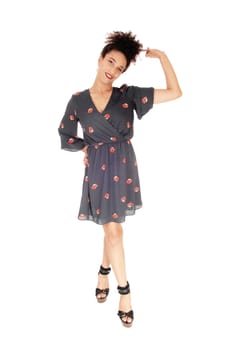 Beautiful young multi-racial woman standing in full length in a black.dress with floral print playing with her black hair in a bun on top of.her head, smiling, isolated for white background.