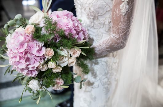 Bride holds big bouquet during ceremony. Couple standing in church for holy matrimony