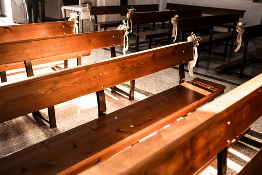 Church decorations before the wedding ceremony. Flowers on the side of the wooden benches at sunset