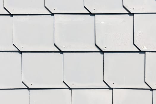 Full-frame view of gray-colored slate roof shingles with hard drop shadows.