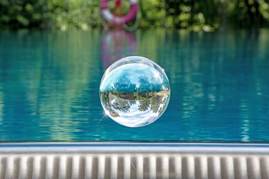 Glass ball hovers over a swimming pool with mirrored cloudy sky and trees