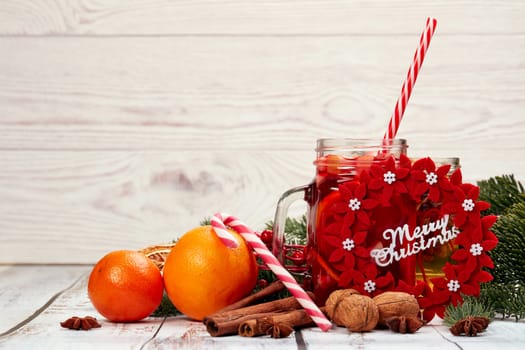 Winter holidays still life with fir tree branch, fruit tea, spices, nuts and oranges on a light wooden background with copy space. New Year and Christmas. Winter vacation.