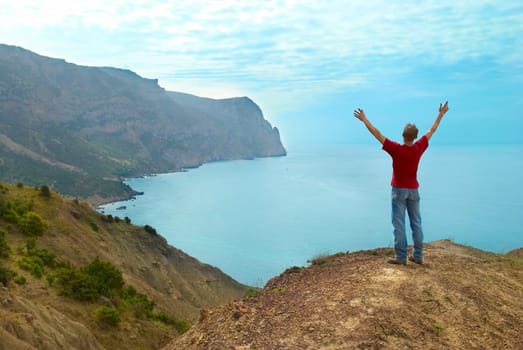 Happy man standing on the cliff with hands up looking at the sea