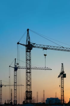 Industrial landscape with silhouettes of cranes on the sunset background