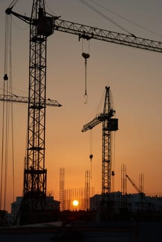 Industrial landscape with silhouettes of cranes on the sunset background