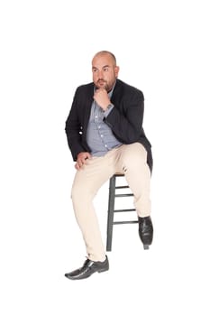 A puzzled middle age business man sitting on a chair with his hand on.his chin, looking for a solution for his problem, isolated for white.background.