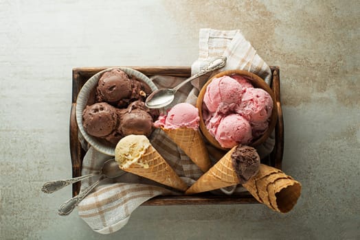 Ice cream scoops with chocolate, strawberry and vanilla flavors, scooped in to waffle cones and bowls