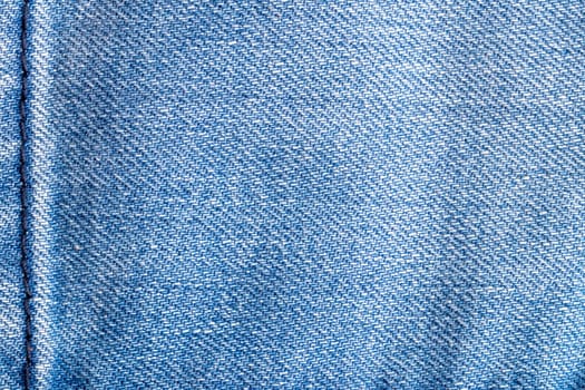 Denim background texture. Close-up of details of empty light blue jeans fabric jean surface with dark blue vertical seam on left side.  Macro. Top view. Beautiful backdrop with space.