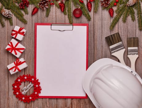Construction hard hat, blank clipboard, gift boxes and Christmas ornament on wooden background. Top view, copy space. New Year and Christmas. For greeting card or advertising. Construction concept