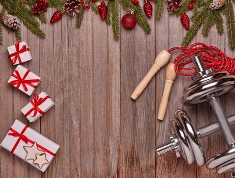 Dumbbells, skipping rope, gift boxes, fir branches and Christmas ornaments on wooden background. Top view with copy space. New Year, Christmas. Fitness, sport and healthy lifestyle concept