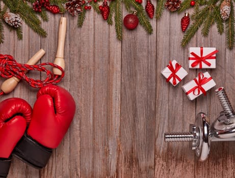 Dumbbells, boxing gloves, gift boxes, fir branches and Christmas ornament on wooden background. Top view with copy space. New Year, Christmas. Fitness, sport and healthy lifestyle concept