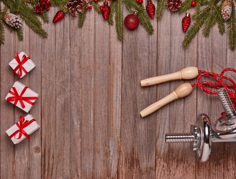 Dumbbells, skipping rope, gift boxes, fir branches and Christmas ornaments on wooden background. Top view with copy space. New Year, Christmas. Fitness, sport and healthy lifestyle concept