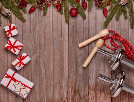 Dumbbells, skipping rope, gift boxes, fir branches and Christmas ornaments on wooden background. Top view with copy space. New Year, Christmas. Fitness, sport and healthy lifestyle concept
