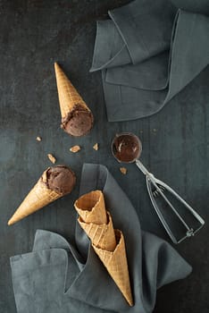 Chocolate ice cream scoops, scooped in to waffle cones with a silver utensil