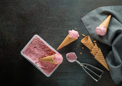 Fresh of soft ice cream or frozen yogurt with berry fruit flavours. Fruit ice cream scoops, scooped out of container in to waffle cones with a silver utensil