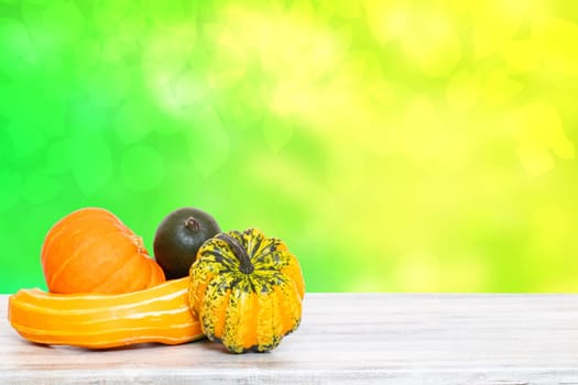 Pile of pumpkins. Close-up of a stack decorative colorful pumpkins on a bright wooden table against abstract blurred natural green yellow background. Space for your product display montage.
