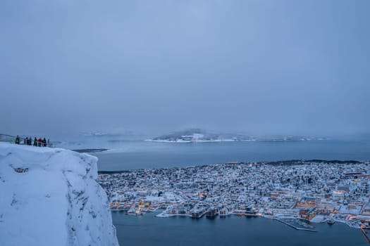 People admiring the view of the city of Tromso in winter from the mountain ledge Storsteinen, 421 m above sea level , Northern Norway