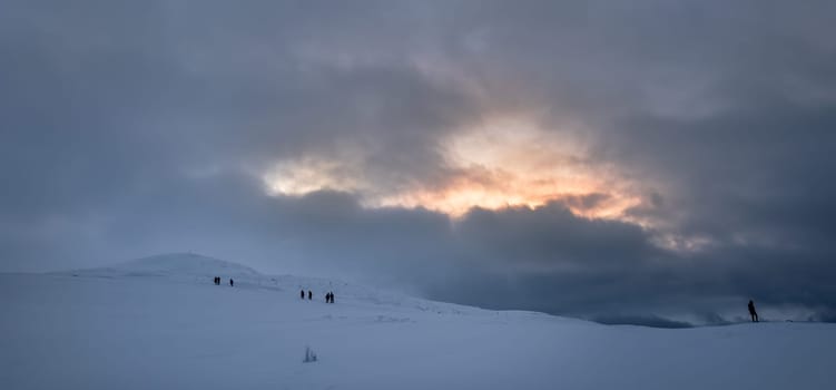 Unidentifiable people walking towards Storsteinen mountain summit and peak in the snow among the wonderful winter scenery, Norway